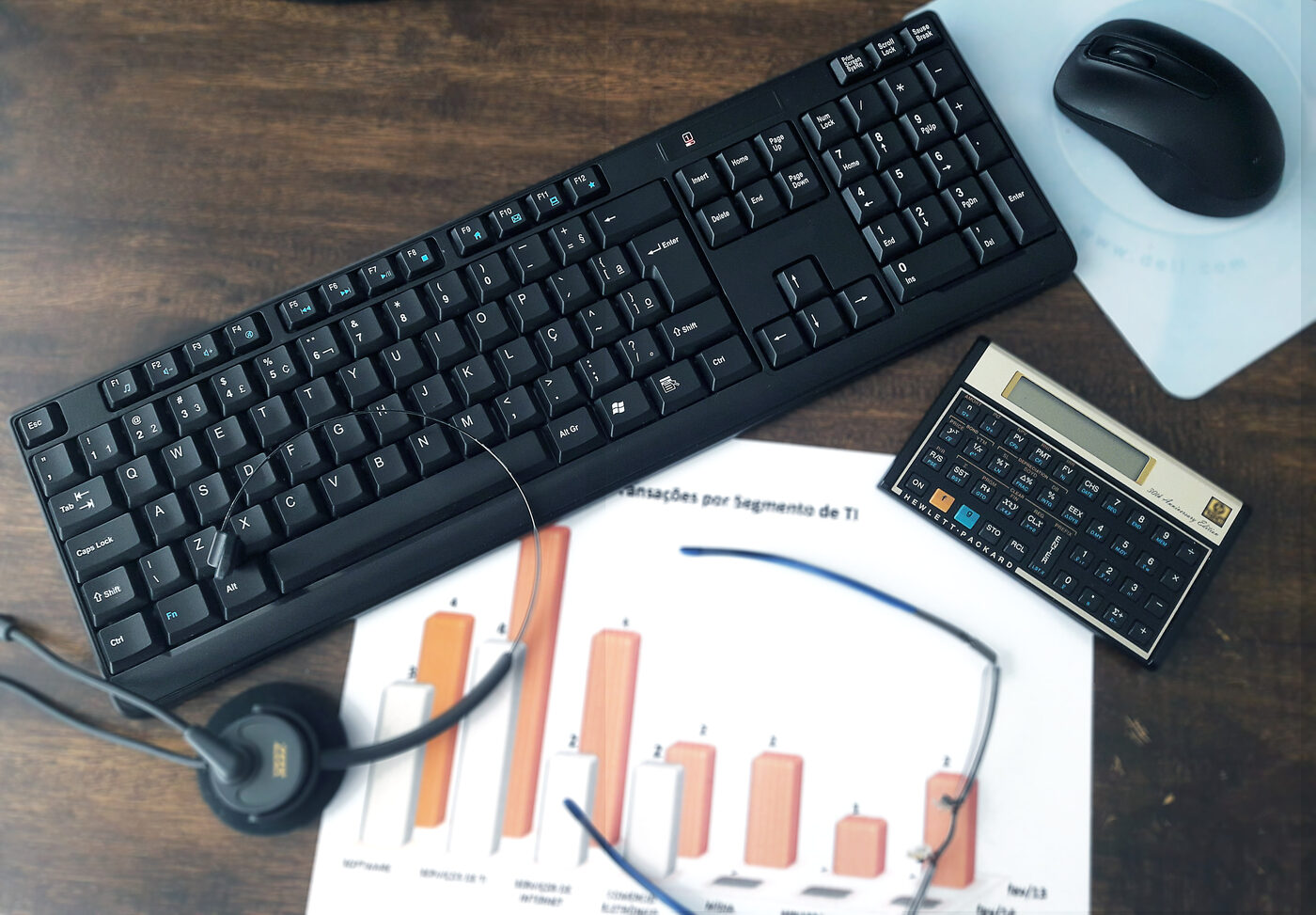 Mesa de trabalho com teclado, headset e relatório de transações por segmento de TI